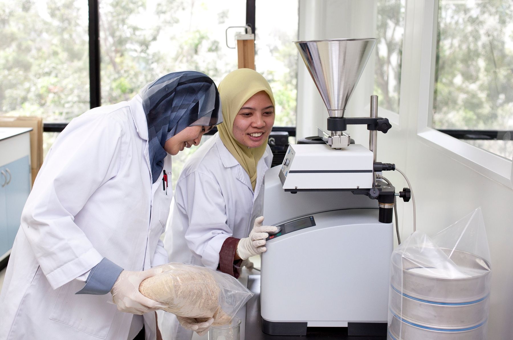 Two Biotropics laboratory staff preparing a root sample at a laboratory mill