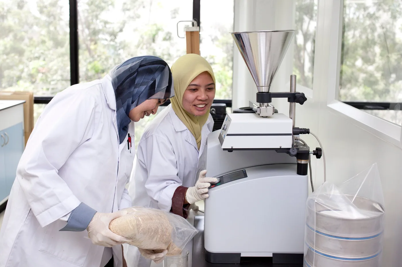 Two Biotropics laboratory staff preparing a powder sample at a laboratory mill